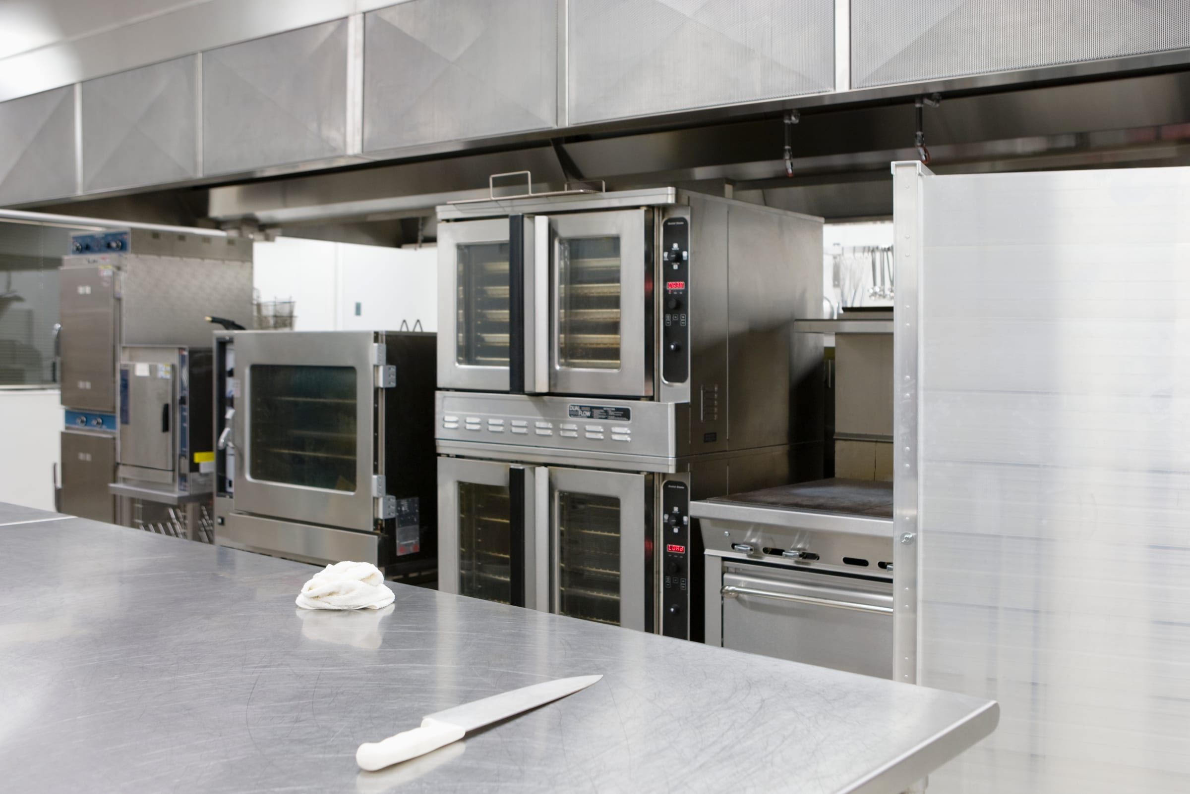 Line cook working a flaming grill on a stainless commercial range